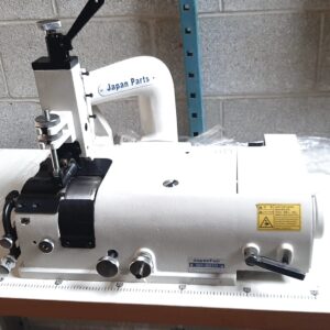 Dixie Tailoring Supply The JapanFuji GT801H Heavy Skiver Sewing Machine, brand new and labeled "Japan Parts" and "JapanFuji," is set on a white table against a concrete wall, featuring visible control knobs and warning labels. Tailoring Supplies