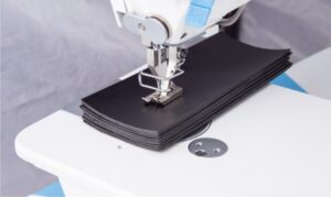 Dixie Tailoring Supply Close-up of the Jack H2 Industrial Walking Foot Sewing Machine stitching multiple layers of black synthetic material on a white table. Tailoring Supplies