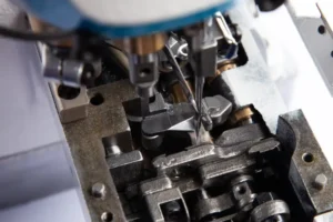 Dixie Tailoring Supply Close-up of the Jack K5 UT01GB Automatic Cylinder Arm Coverstitch Industrial Sewing Machine's needle and presser foot stitching fabric. Tailoring Supplies