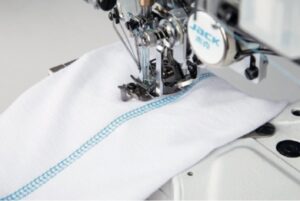 Dixie Tailoring Supply Close-up of the Jack W4 UT01 Automatic Flat Bed Coverstitch Industrial Sewing Machine stitching blue thread on white fabric. Tailoring Supplies
