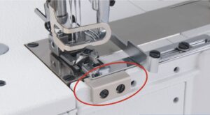 Dixie Tailoring Supply Close-up of the presser foot and needle area on the Jack W4 UT01 Automatic Flat Bed Coverstitch Industrial Sewing Machine, highlighting a beige metal part attached with two black screws. Tailoring Supplies