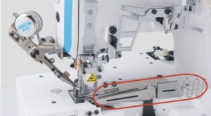 Dixie Tailoring Supply Close-up view of the Jack W4 UT01 Automatic Flat Bed Coverstitch Industrial Sewing Machine, highlighting the needle area and metal fabric guide attachment in red. Tailoring Supplies
