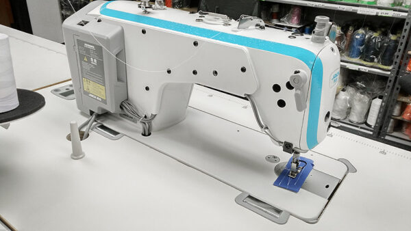 Dixie Tailoring Supply A white and blue JACK A4 Fully Automatic Industrial Sewing Machine sits on a table, surrounded by colorful spools of thread, showcasing the precision and quality synonymous with Tailor Products. Tailoring Supplies