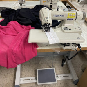 Dixie Tailoring Supply In a bustling tailoring store, the Japanfuji Blind Stitch Industrial Sewing Machine expertly stitches white fabric amidst an array of black and pink fabric pieces. Tailoring Supplies