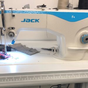 Dixie Tailoring Supply The JACK F4 Sewing Machine, with its sleek blue and white design, is perfect for tailoring stores. It sits on a table amidst threads and fabric scraps, making it an essential addition to your collection of tailor products. Tailoring Supplies