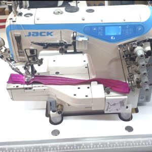 Dixie Tailoring Supply In a bustling tailoring store, the JACK K4 UT Automatic Coverstitch Sewing Machine with its blue and white design expertly stitches a purple zipper onto fabric. Tailoring Supplies