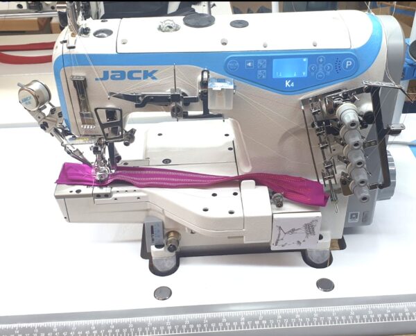 Dixie Tailoring Supply In a bustling tailoring store, the JACK K4 UT Automatic Coverstitch Sewing Machine with its blue and white design expertly stitches a purple zipper onto fabric. Tailoring Supplies