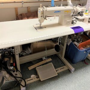 Dixie Tailoring Supply In a busy tailoring store, the JUKI DDL 5600N heavy lockstitch double-capacity hook sewing machine sits on a sturdy table, surrounded by essential crafting tools and supplies for tailor products. Tailoring Supplies