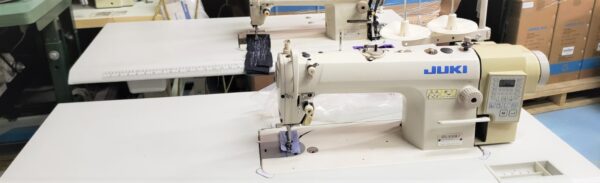 Dixie Tailoring Supply The JUKI DDL 8100-7 used industrial automatic single needle sewing machines sit on a worktable in a factory, surrounded by boxes and equipment, capturing the essence of a bustling tailoring store. Tailoring Supplies