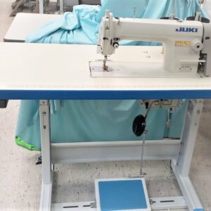 Dixie Tailoring Supply A Juki DDL 8700 brand new industrial single needle sewing machine on a stand with light blue fabric draped over it, perfectly set in a bustling tailoring store. Tailoring Supplies