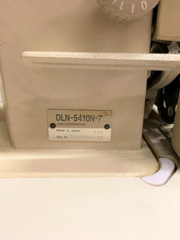 Dixie Tailoring Supply Close-up of a sewing machine label: "JUKI DLN 5410N-7, Juki Corporation, Made in Japan," with manufacturing number "203BC00140." Ideal for any tailoring store in need of top-quality products. Tailoring Supplies