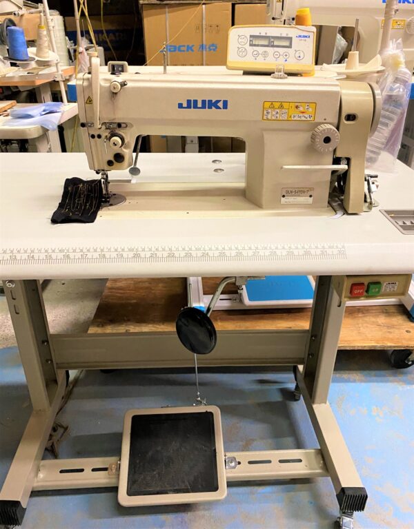 Dixie Tailoring Supply The JUKI DLN 5410N-7 is a used 1-needle, needle-feed lockstitch machine on a worktable with foot pedals and various controls, perfect for any tailoring store looking to expand its range of products. Tailoring Supplies