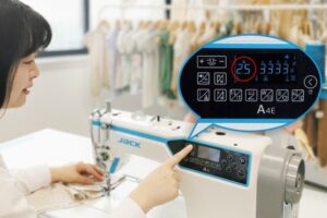 Dixie Tailoring Supply A person uses the Jack A4E Computerized Lockstitch Machine with Electronic Stitch Length Control, pressing a button on its digital panel displaying stitch options and a highlighted 2.5 setting. Tailoring Supplies