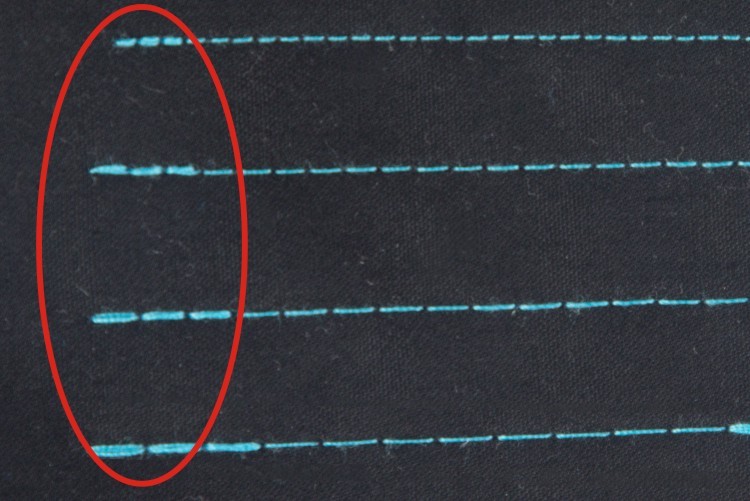 Dixie Tailoring Supply Close-up of black fabric showing horizontal blue stitches made by the Jack A4E Computerized Lockstitch Machine with Electronic Stitch Length Control; a red oval highlights irregular or missing stitches. Tailoring Supplies
