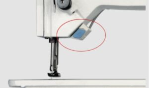Dixie Tailoring Supply Close-up of the needle area on the JACK 20U Zigzag Industrial Single Needle Sewing Machine, highlighting a blue rectangular button with a red circle. Tailoring Supplies