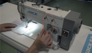 Dixie Tailoring Supply Someone adjusts a lever on a JACK 20U Zigzag Industrial Single Needle Sewing Machine, with fabric under the needle and a red circle emphasizing the lever. Tailoring Supplies