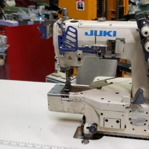 Dixie Tailoring Supply A JUKI MF 7823 Industrial Coverstitch Sewing Machine sits on a table in a busy tailoring shop, with various tools and tailor products in the background. Tailoring Supplies