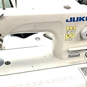 Dixie Tailoring Supply A white Hakari Automatic Industrial Single Needle Sewing Machine sits on a worktable, featuring control dials, warning labels, and a metal plate beneath the needle. Tailoring Supplies