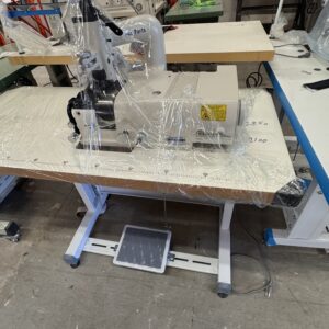 Dixie Tailoring Supply A Kingmax 801 Brand New Skiver Sewing Machine, wrapped in plastic, sits on a table in a workshop with various tools and equipment visible in the background. Tailoring Supplies