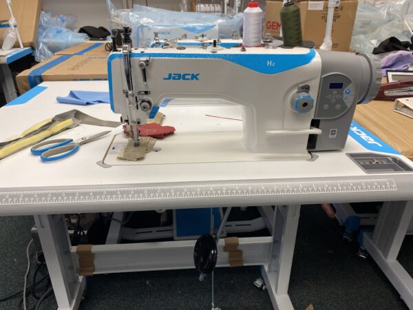 Dixie Tailoring Supply A JACK H2 Industrial Walking Foot Sewing Machine sits on the table, surrounded by scissors, thread, and fabric—ideal for showcasing premium tailor products in a bustling tailoring store. Tailoring Supplies