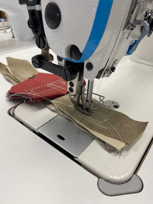 Dixie Tailoring Supply In a bustling tailoring store, a close-up features the JACK H2 INDUSTRIAL WALKING FOOT SEWING MACHINE expertly stitching multiple layers of red and beige fabric. The white thread contrasts sharply as it weaves through, highlighting the precision and finesse of tailor products. Tailoring Supplies
