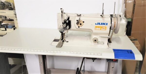 Dixie Tailoring Supply A JUKI DNU 1541 USED industrial sewing machine sits on a work table in the tailoring store, with a ruler printed on the edge and a blue organizer attached, showcasing essential tailor products. Tailoring Supplies