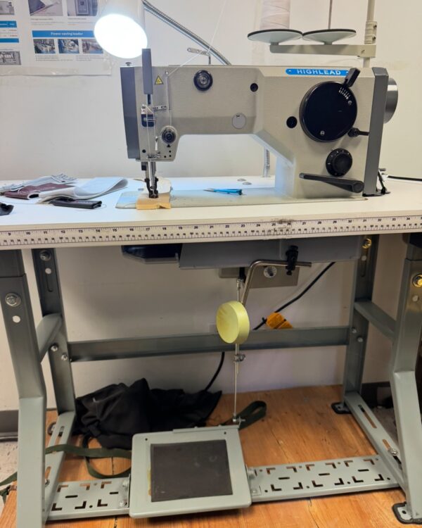 Dixie Tailoring Supply Industrial sewing machine on a worktable with foot pedal, spool of thread, and various sewing materials and tools nearby. Tailoring Supplies