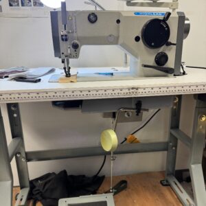 Dixie Tailoring Supply Industrial sewing machine on a worktable with thread spools, a lamp, tools, and a foot pedal beneath. Tailoring Supplies