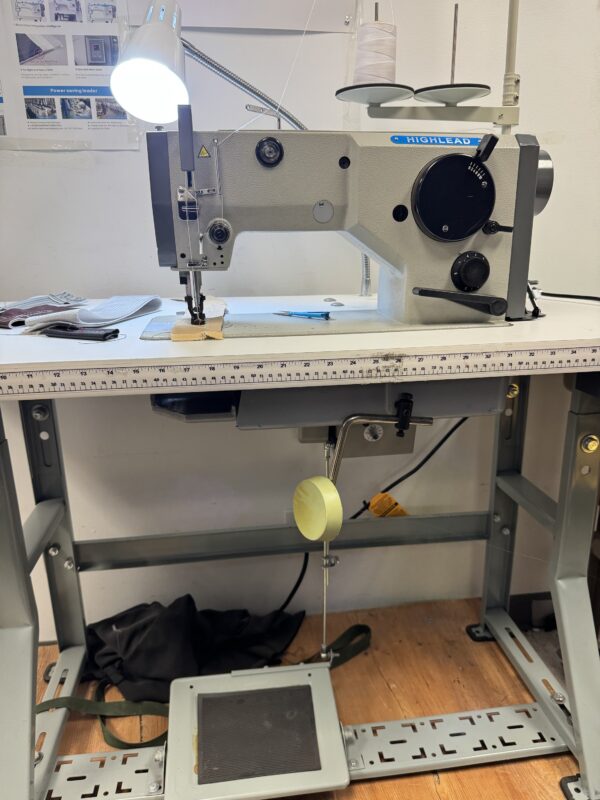 Dixie Tailoring Supply Industrial sewing machine on a worktable with thread spools, a lamp, tools, and a foot pedal beneath. Tailoring Supplies