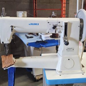 Dixie Tailoring Supply Industrial Juki sewing machine stitching a piece of tan leather with visible thread and patterns in a workshop setting. Tailoring Supplies